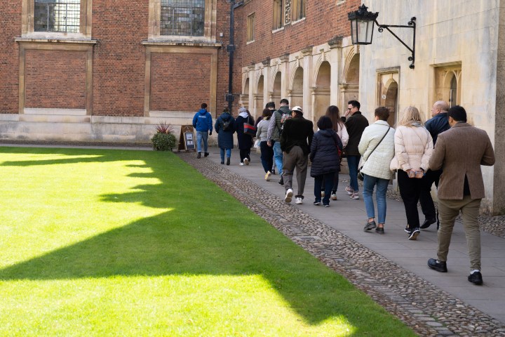 A group of people walking on a paved path by a historic brick building.