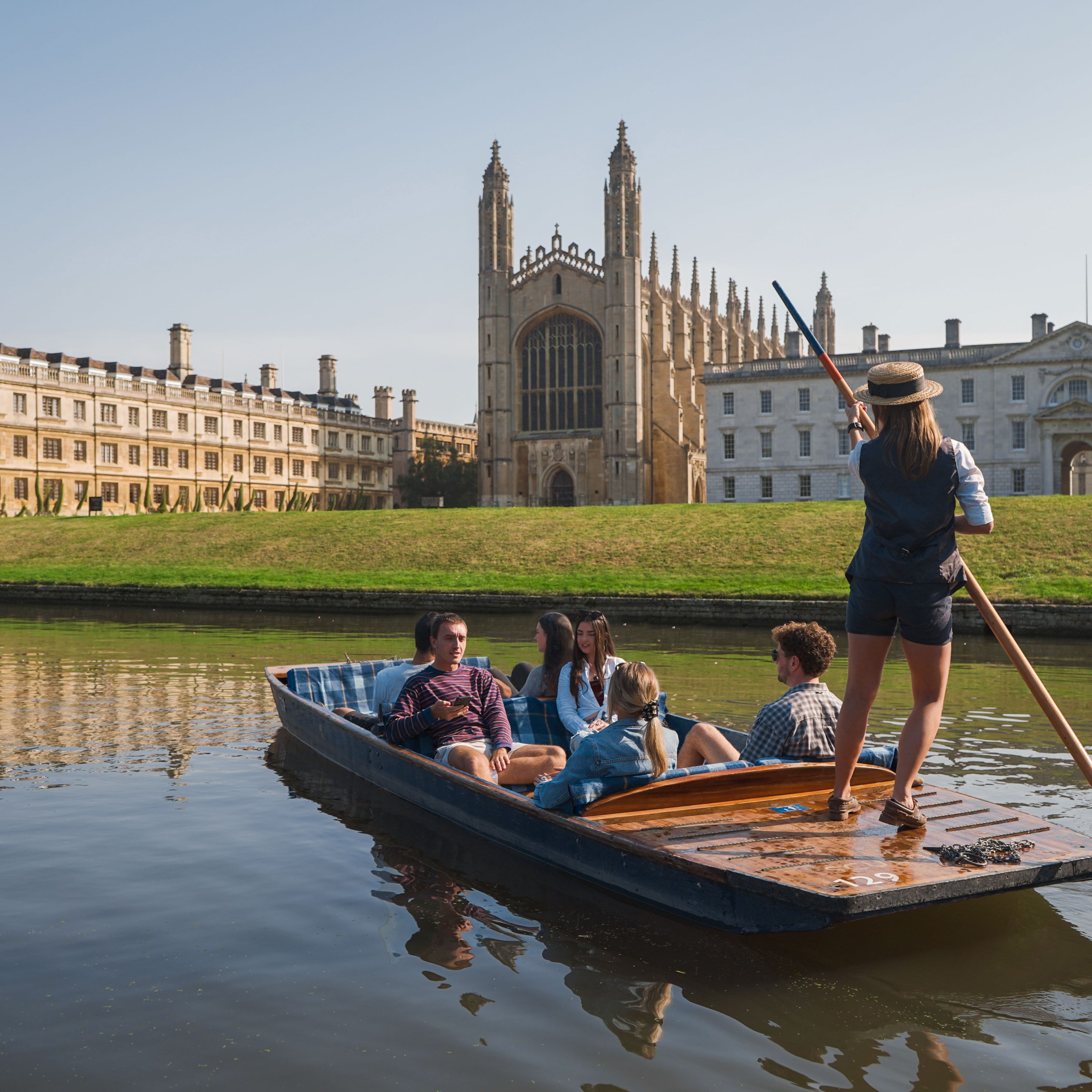Group punting on a river by historic buildings under a clear sky.