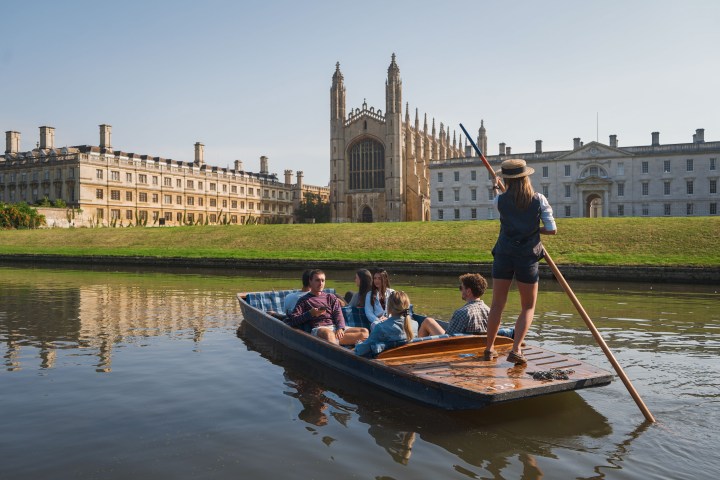 Group punting on a river by historic buildings under a clear sky.