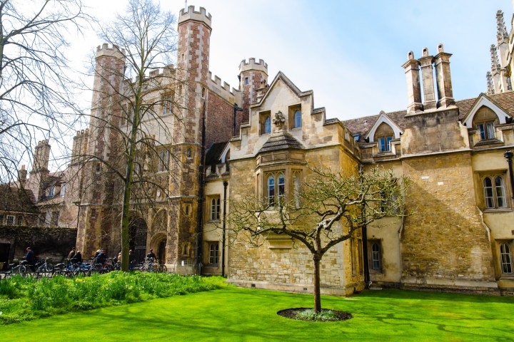 Historical stone building with towers and a courtyard with green grass and trees.