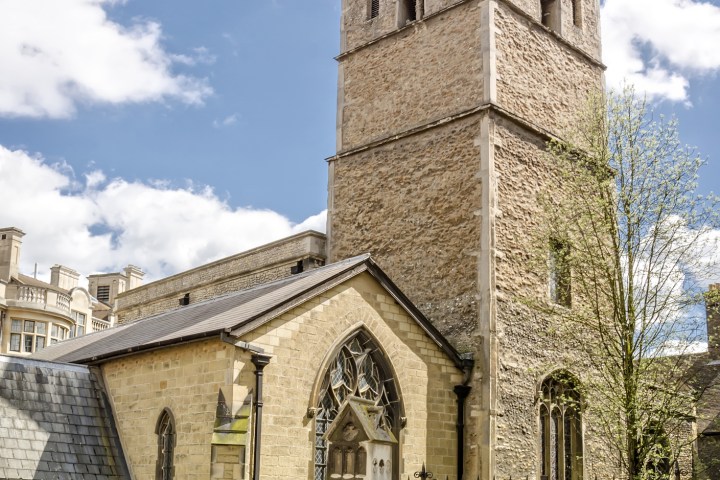 Historic stone church with a tower, bicycles, and a fence under a partly cloudy sky.