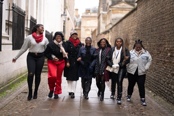 Group of seven people walking arm-in-arm down a cobblestone street.