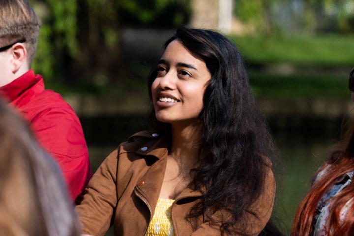 Smiling person in brown jacket outdoors, surrounded by people.